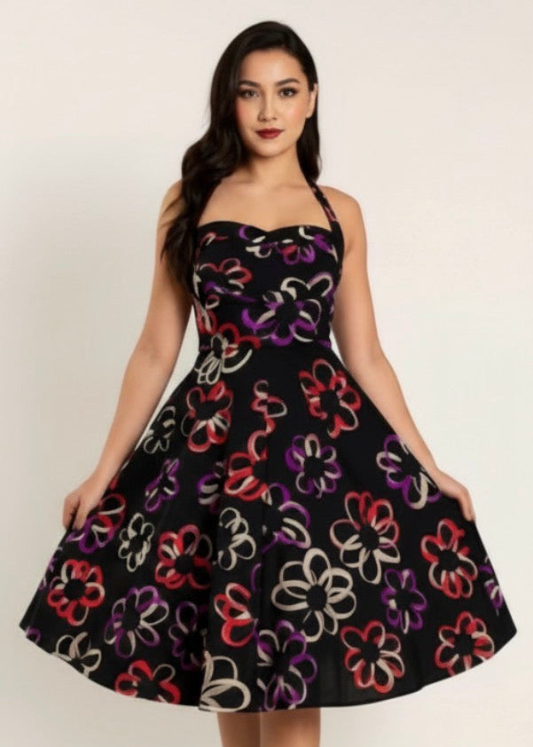 A woman modeling a black strapless fit-and-flare dress with a colorful floral pattern in red, purple, white, and orange, paired with black strappy heels against a plain light background.