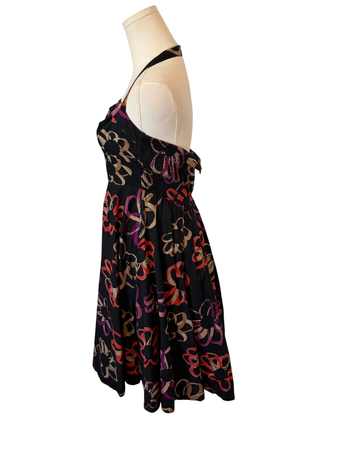 A sleeveless halter-neck dress displayed on a cream mannequin torso against a plain white background. The dress has a black base with a colorful abstract floral pattern in red, orange, purple, and beige.