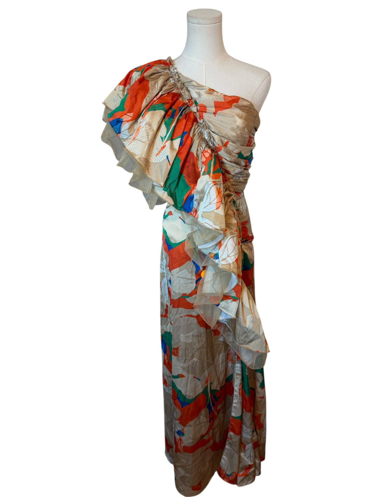 A one-shoulder maxi dress with a dramatic ruffled neckline, featuring an abstract multicolor print on a beige base. The dress is displayed on a white mannequin torso against a plain white background.