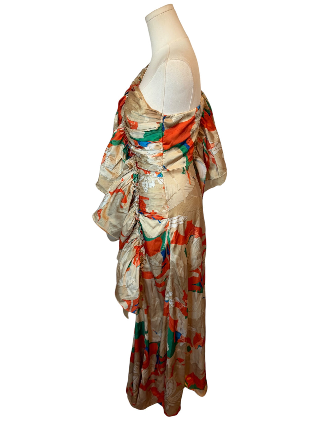 A draped, one-shoulder maxi dress with an abstract painterly pattern in orange, green, blue, and beige, displayed on a cream mannequin torso against a white background.
