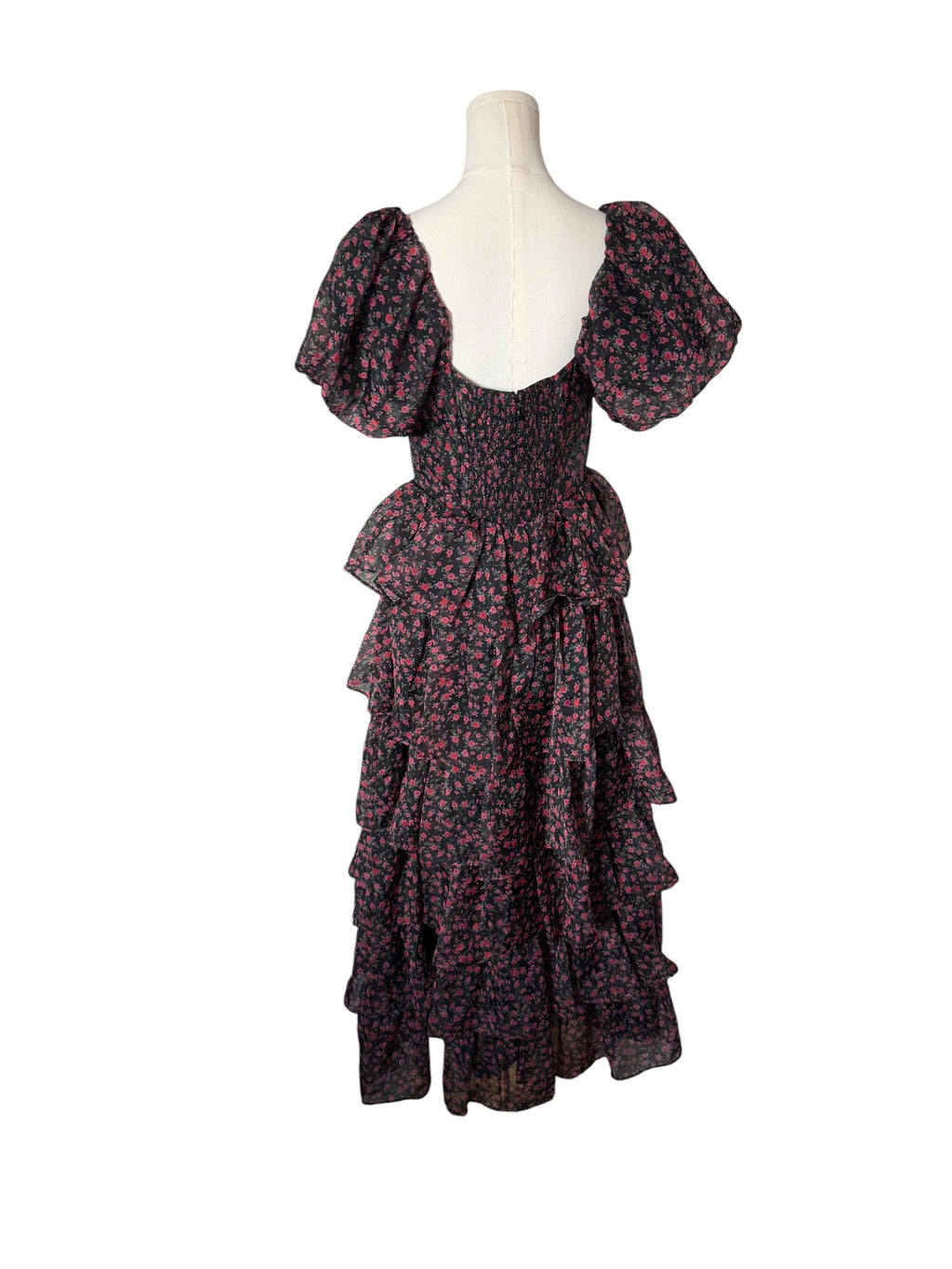 A dark floral tiered dress with puff sleeves and a smocked bodice, displayed on a cream mannequin torso against a plain white background.