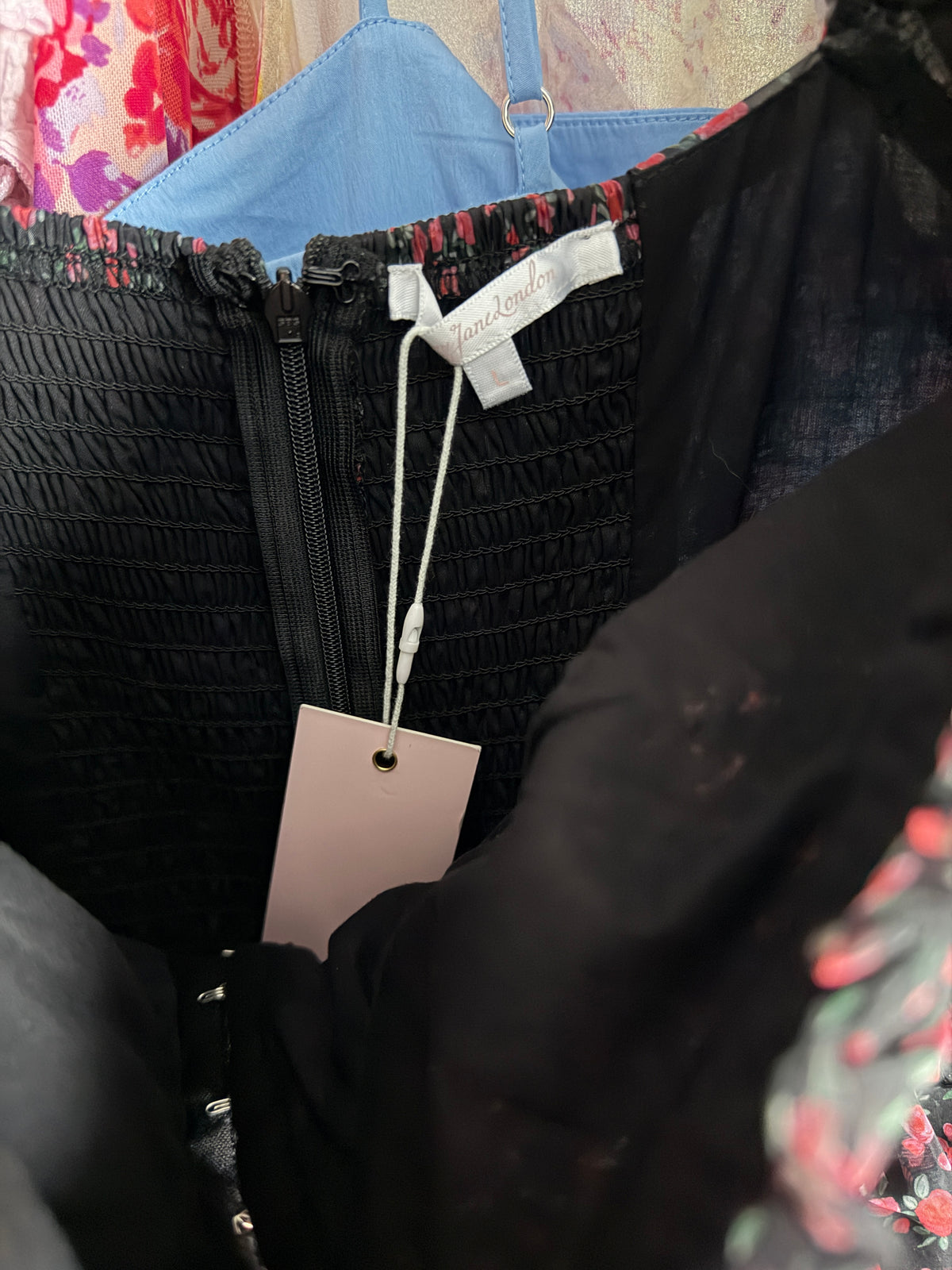 A close-up of a black smocked zip-front garment with a white hangtag and a white brand label that reads 