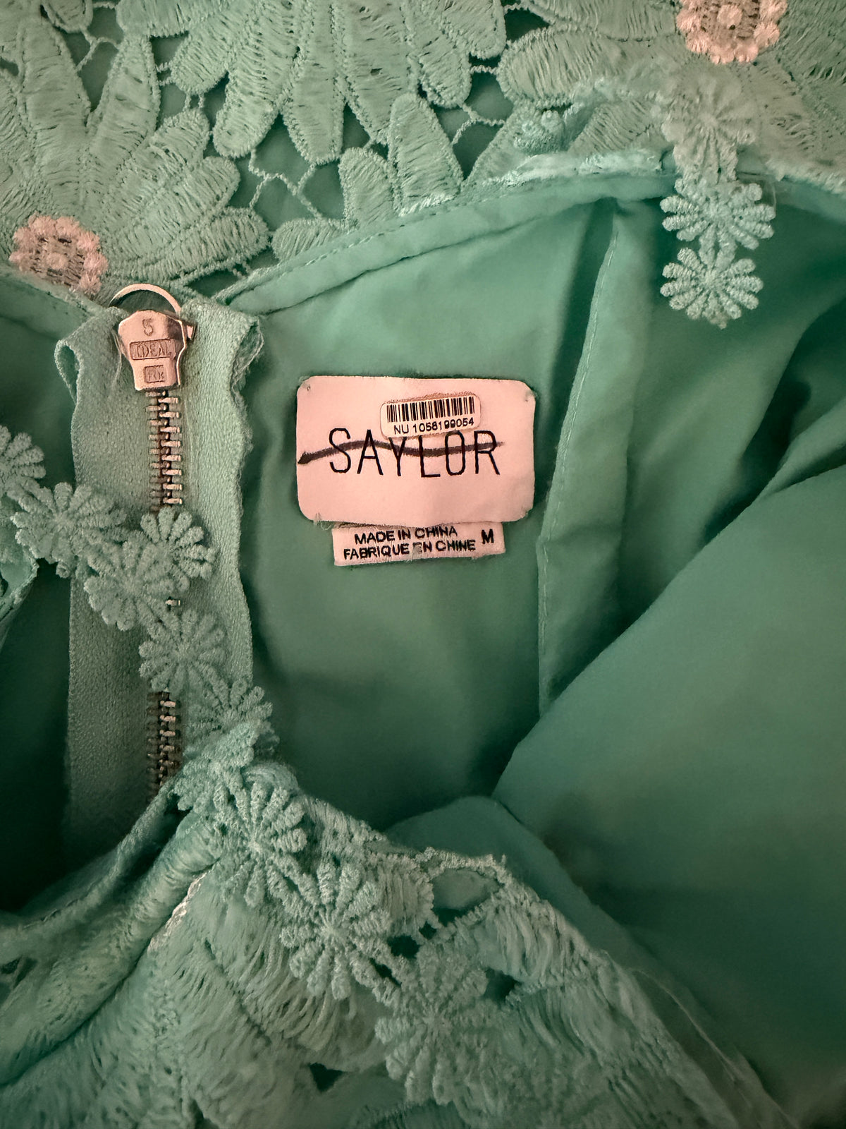 Close-up of a mint green garment with floral lace trim and a visible sewn-in label reading SAYLOR.