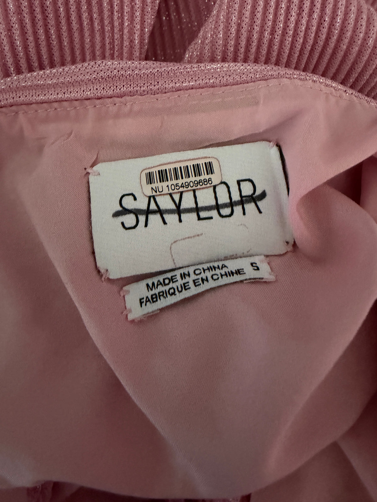 Close-up of a pink garment's interior label area, showing a white sewn-in label with the brand name 'SAYLOR' and another tag reading 'MADE IN CHINA FABRIQUE ECHTINE 5'.